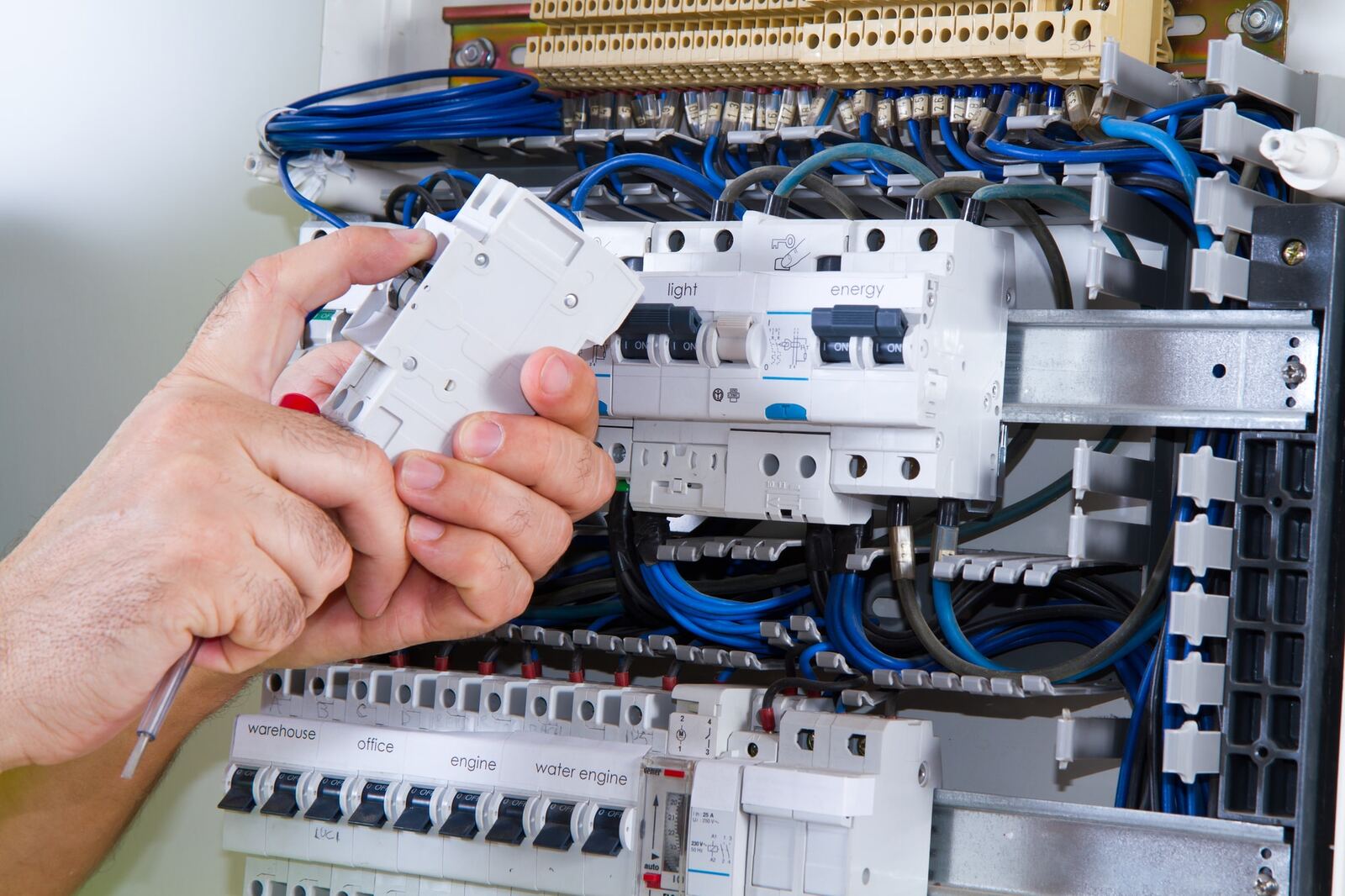 An electrician holding a new RCBO module above a labelled DB with light and energy circuits