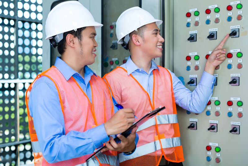 Two contractors in safety vests inspecting an industrial control panel with status indicators