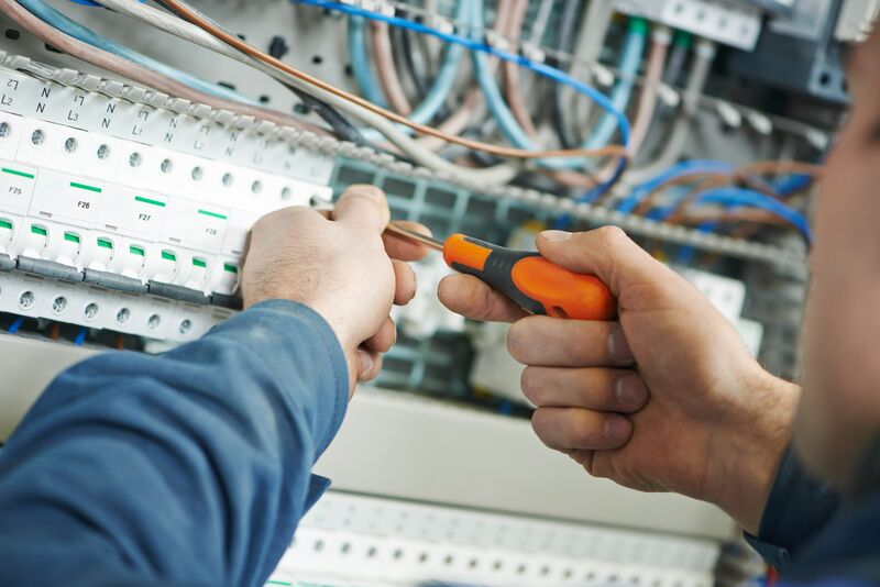 A licensed electrician tightening a terminal inside a labelled distribution board